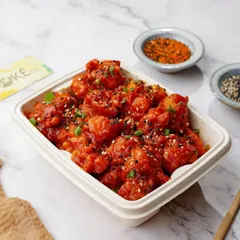 Crispy bang bang cauliflower in a takeaway container, shot on a clean marble background.