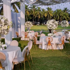 A beautiful daytime view of the reception setup on the lawns of the Taj Exotica, Goa. The crisp white tables are adorned with large floral centerpieces, creating an atmosphere of fresh, natural elegance against the backdrop of palm trees.
