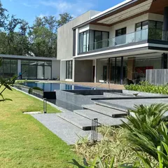 The expansive view of a modern Delhi farmhouse, where a pristine swimming pool and manicured lawn meet contemporary architecture. This project showcases our ability to create seamless transitions between indoor comfort and outdoor splendor, featuring clean lines and lush greenery.