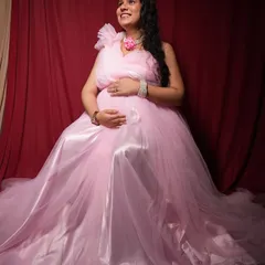 A happy and radiant mom-to-be seated in a beautiful pink tulle gown against a classic red backdrop in my studio. This is a popular choice for a timeless maternity photo.