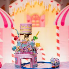 A magnificent Candyland cake that is a true work of art. It features multiple tiers, a miniature train, and is adorned with colorful candy decorations.