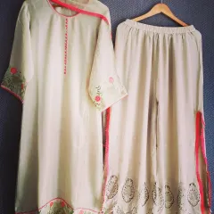 An off-white kurta and palazzo set detailed with delicate floral embroidery and a bright pink border. The palazzo pants feature intricate cutwork, adding a unique and modern touch to this classic festive outfit.