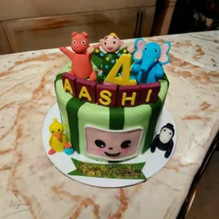 A vibrant Cocomelon theme cake, perfect for a toddler's birthday. This design features edible figurines of JJ and his animal friends, set against a cheerful green-striped cake.