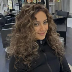 An elegant color transformation on naturally curly hair. The soft highlights are carefully placed to enhance the dimension and shape of her beautiful curls.