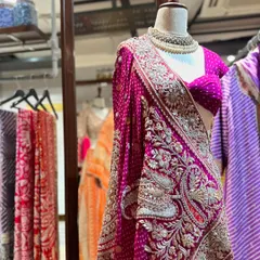A saree is always a classic choice. This piece stands out with its heavily embroidered peacock motifs on the pallu, set against a deep magenta bandhani fabric.