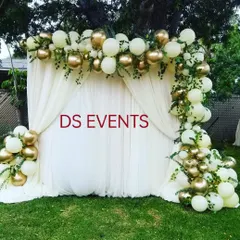 An elegant outdoor balloon decoration. This asymmetrical arch uses white and chrome gold balloons with fresh greenery tucked in, creating a sophisticated and modern photo backdrop for any celebration.