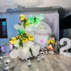 A beautiful birthday setup with a white, green, and gold color scheme. The decoration features a personalized backdrop, a neon sign, an elephant cutout, and a light-up number '2'.