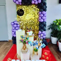 A stylish birthday setup with a gold shimmer wall, framed by a purple and black balloon arch. Personalized elements like photos make the celebration extra special.
