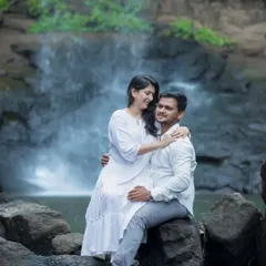 A gentle and loving pose from a waterfall maternity shoot. The mother-to-be sits on her partner's lap, her arm around him, as they both smile, creating a beautiful portrait of togetherness in a tranquil setting.