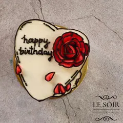 A close-up of the hand-piped comic-style art on the heart-shaped bento cake. The delicate red rose and falling petals add a touch of romance.