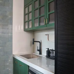 Another view of the green kitchen, showcasing the fluted glass shutters on the upper cabinets, the matte black faucet, and the full-body textured tiles on the wall.