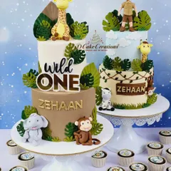 A pair of our popular jungle-themed birthday cakes. These "Wild One" creations feature hand-sculpted fondant animals like elephants, giraffes, and monkeys, surrounded by tropical leaves, making them perfect for a safari adventure party.