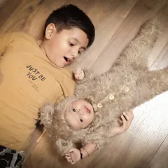 An adorable and playful interaction between siblings. An older brother lies on the floor, looking with surprise and delight at his baby sibling dressed in a cute teddy bear outfit.