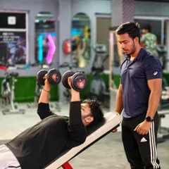 A trainer supervises a client performing an incline dumbbell press. We keep a close watch on your form to maximize muscle engagement and prevent injury.