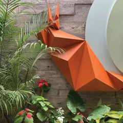 A close-up of the snail's form, showing the sharp, geometric folds of the metal contrasting with the soft, organic shapes of the surrounding plants. This juxtaposition is central to the piece's impact.