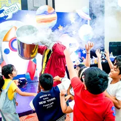 An interactive science show where kids gather around in excitement as the performer creates a cloud of smoke with a safe chemical reaction.