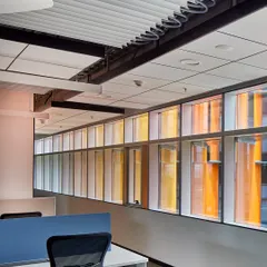 Inside the Infosys office, the colorful facade fins create a pleasant, diffused light. The design optimizes the floorplate for work areas, with exposed ceilings and efficient layouts that ensure both spatial generosity and clarity in circulation.