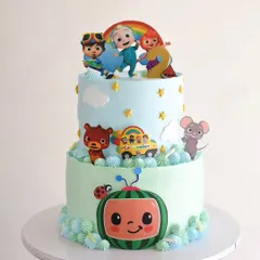 A cheerful two-tiered Cocomelon cake, perfect for a toddler's birthday. The design features edible character cutouts, a soft blue and green color scheme, and playful details like clouds and stars.