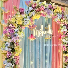 A close-up of the pastel floral arch and 'Mehndi' neon sign, highlighting the soft and dreamy color combination.