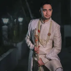 A stylish portrait of the groom in his off-white sherwani, captured in the soft evening light. The mood is classic and contemplative.