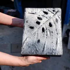 This sculptural tile, held by a workshop participant, shows the dramatic crackle and smoky effects achieved through Raku firing. The holes and textures interact with the unpredictable glaze.