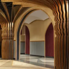 A detail of the custom-fabricated columns at Nishtara, which flow upward into the vaulted ceiling. The rhythmic, undulating form of the rubberwood profiles softens the grand scale of the hall and adds a layer of intricate craftsmanship.