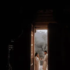 A beautifully framed shot of the couple standing in the doorway of an old heritage building. The dark foreground creates a sense of intimacy and timelessness.