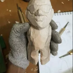 Here I am holding a figurine in the middle of the carving process. I wear a protective glove while using my tools to carefully shape the wood, ensuring every detail is just right before moving on to sanding and painting.