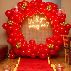 The perfect proposal setup. This decoration features a large ring of red balloons, a 'Will you marry me?' neon sign, and a red carpet aisle lined with candles, creating an unforgettable moment.