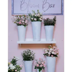 The setup for our Bloom Bar, featuring a variety of fresh flowers in white tins against a pink backdrop. The simple, elegant presentation is both beautiful and functional.