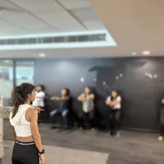 Coaching a group of employees through a squat. Fitness in the office doesn't require a gym. Simple bodyweight movements can make a huge difference in your day.