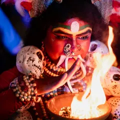Another angle of the Kali performer, this time focusing on the interaction with the sacred fire. The lighting highlights the detailed makeup and skull decorations.