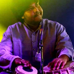 A close up shot capturing a moment of soulful expression during a live concert. The warm, yellow and purple stage lighting adds to the mood of the performance.