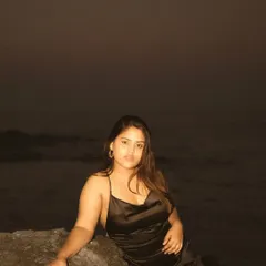 A night portrait on a rocky beach, using a subtle flash to illuminate the subject against the dark ocean. The result is a quiet, intimate, and slightly mysterious image.