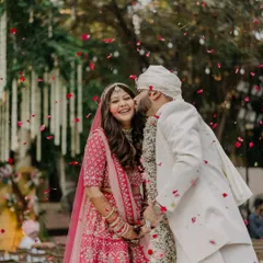 A happy couple showered with rose petals. The bride's hair is styled in soft, open curls, a romantic choice for her pink lehenga.