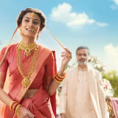 This image for a Tanishq Rivaah campaign showcases a complete bridal look with layered gold necklaces, jhumkas, and a nath. The styling is traditional yet feels light and airy, set against a soft-focus outdoor wedding backdrop.