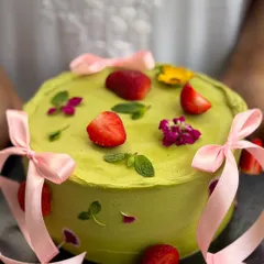 A custom-decorated Matcha Raspberry cake, adorned with fresh strawberries, edible flowers, and pink ribbons for an elegant, bespoke finish.