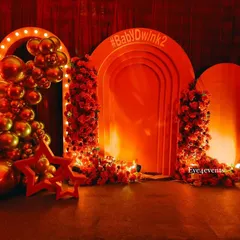 A glamorous Bollywood night themed backdrop, glowing in warm orange light. The setup includes arched panels, marquee lights, and columns of red flowers, with a custom hashtag for the event, creating a perfect movie premiere vibe.