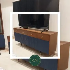 This TV unit combines a rich wood grain with a deep blue fluted finish on the cabinet doors. The tapered legs with brass tips add a mid-century modern touch, creating a piece that is both stylish and highly functional.