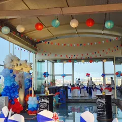 An overview of the party venue, showing the red, white, and blue color scheme carried through with hanging paper lanterns, pennant banners, and balloon arrangements, all complementing the main stage.