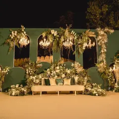 An elegant reception stage set against a deep green backdrop, adorned with white florals and crystal chandeliers. This design combines classic opulence with modern sophistication for a timeless look.