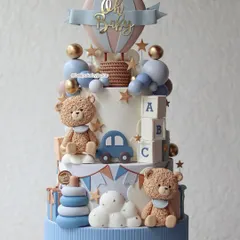 An elaborate and adorable two-tiered cake perfect for a baby shower. It's packed with cute details like teddy bears, a hot air balloon, a car, and alphabet blocks.
