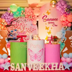 Sanveekha's first birthday combined butterflies and fairies for a whimsical celebration. The setup includes a cherry blossom backdrop, fairy wing cutouts, and a pastel balloon arch, creating a dreamy and colorful scene.