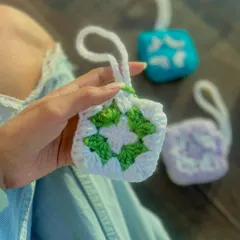 This handmade AirPods pouch features a classic green and white granny square design. It's a stylish way to protect your earphones, with a small loop that makes it easy to attach to your bag or keys.