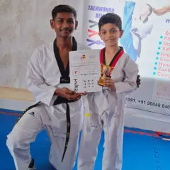 A coach congratulates a young student on his successful belt promotion. He proudly holds his certificate and trophy, marking a new stage in his training.