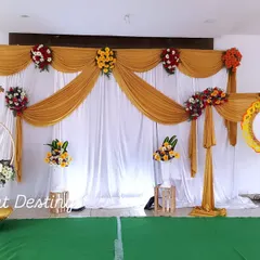 This naming ceremony decor features a unique crescent-moon cradle and a separate name reveal stand. The backdrop is created with simple white and gold drapes, accented with fresh flower bouquets.