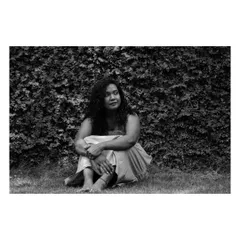 A contemplative black and white portrait. The subject is seated in the grass, and the monochrome tones emphasize the peaceful, natural setting.