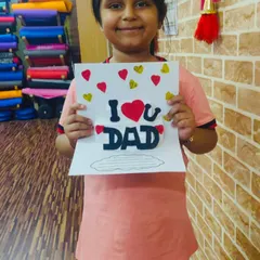 A proud student holding up her handmade "I Love U Dad" card. Our craft sessions often focus on creating things for special occasions like Father's Day.
