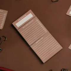 A close-up of a daily intention and self-care checklist notepad. Styled with matching office supplies on a brown background, this shot emphasizes organization and mindfulness.