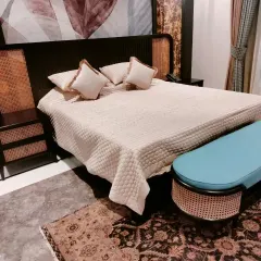 A full view of a bedroom set we designed, featuring a bed with a dark wood frame and caned headboard panels. The look is completed with matching caned bedside tables and a stylish upholstered ottoman at the foot of the bed.